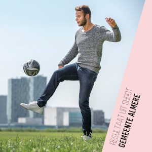 Resultaat fotoshoot voor Gemeente Almere – fotomodel man houdt voetbal hoog met skyline van Almere op de achtergrond